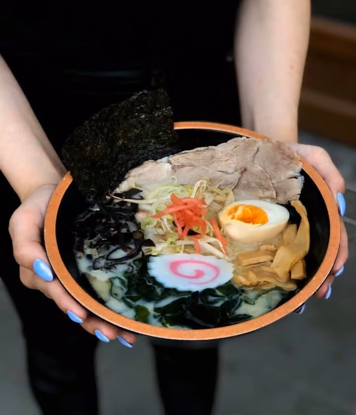 Miska ramenu z jajkiem i narutomaki trzymana w dłoniach